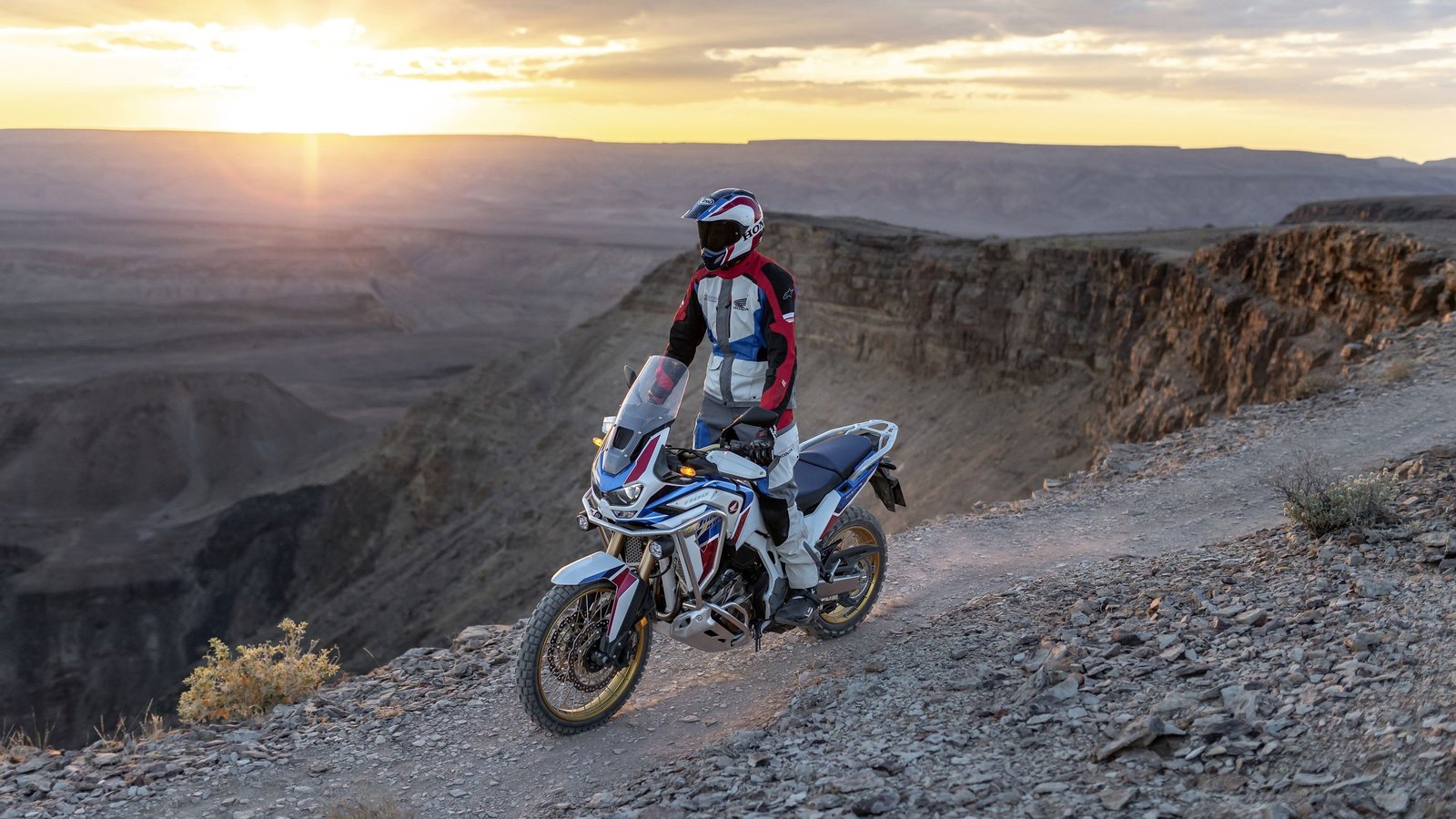 Rider Honda Africa Twin sur crête rocheuse au coucher de soleil au Maroc